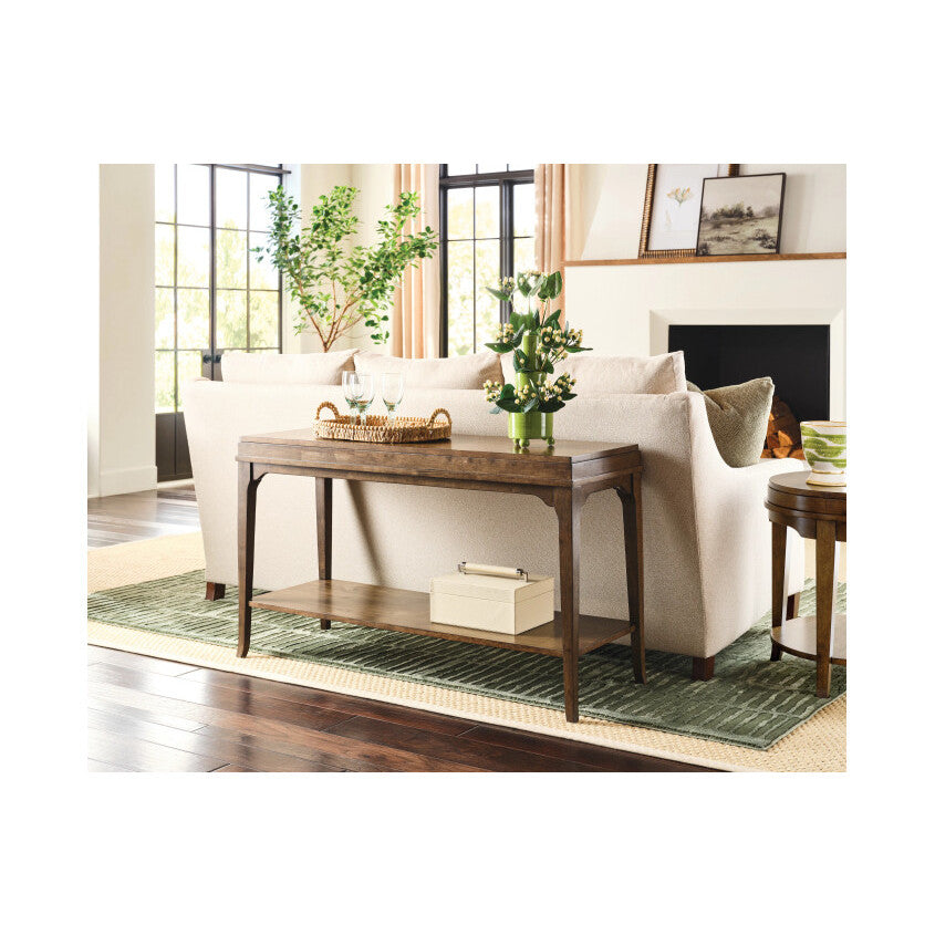 Sofa table behind beige couch with vase, tray and decor in a bright living room.