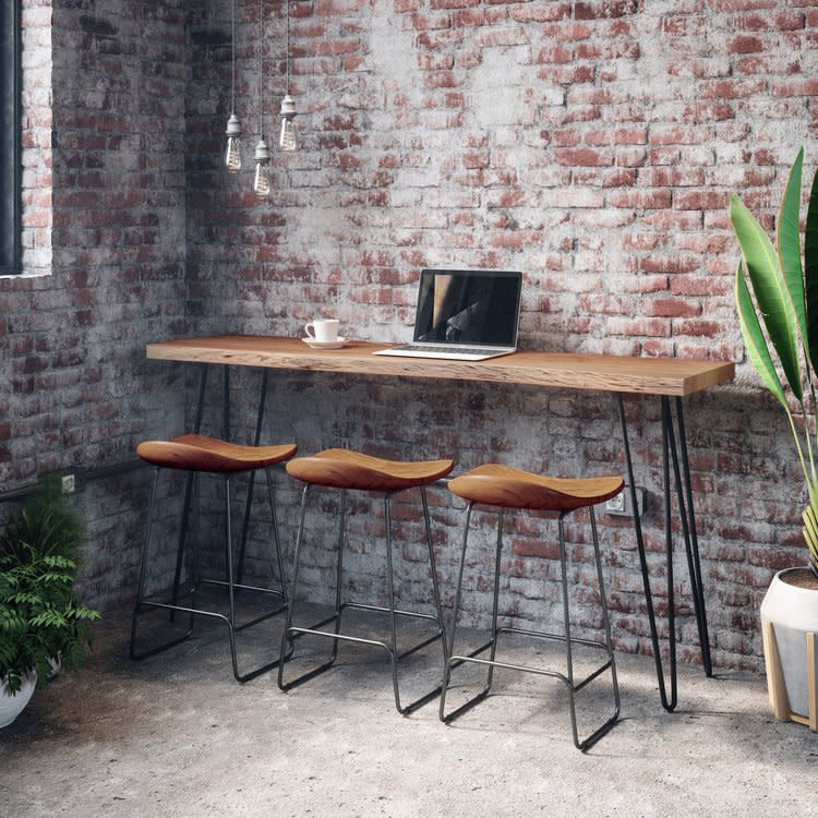 Modern high table with three bar stools and a laptop, set against an exposed brick wall.